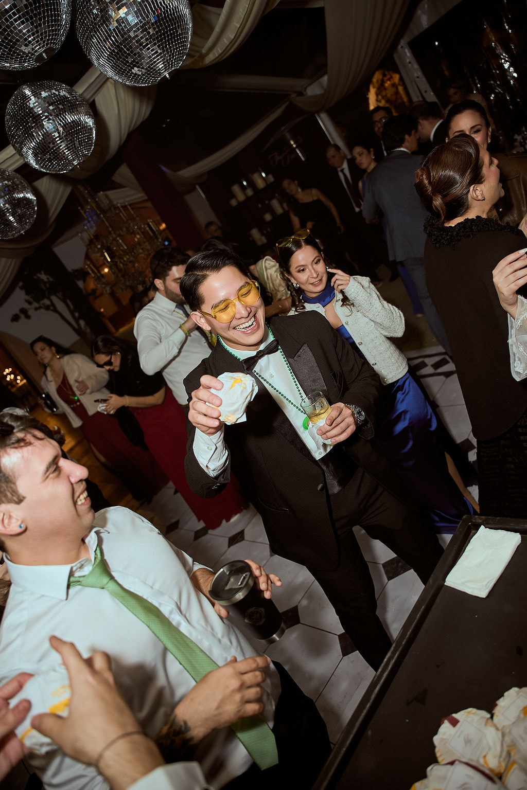 Invitados riéndose y brindando en plena fiesta, sin posar, con la luz cálida del salón de noche