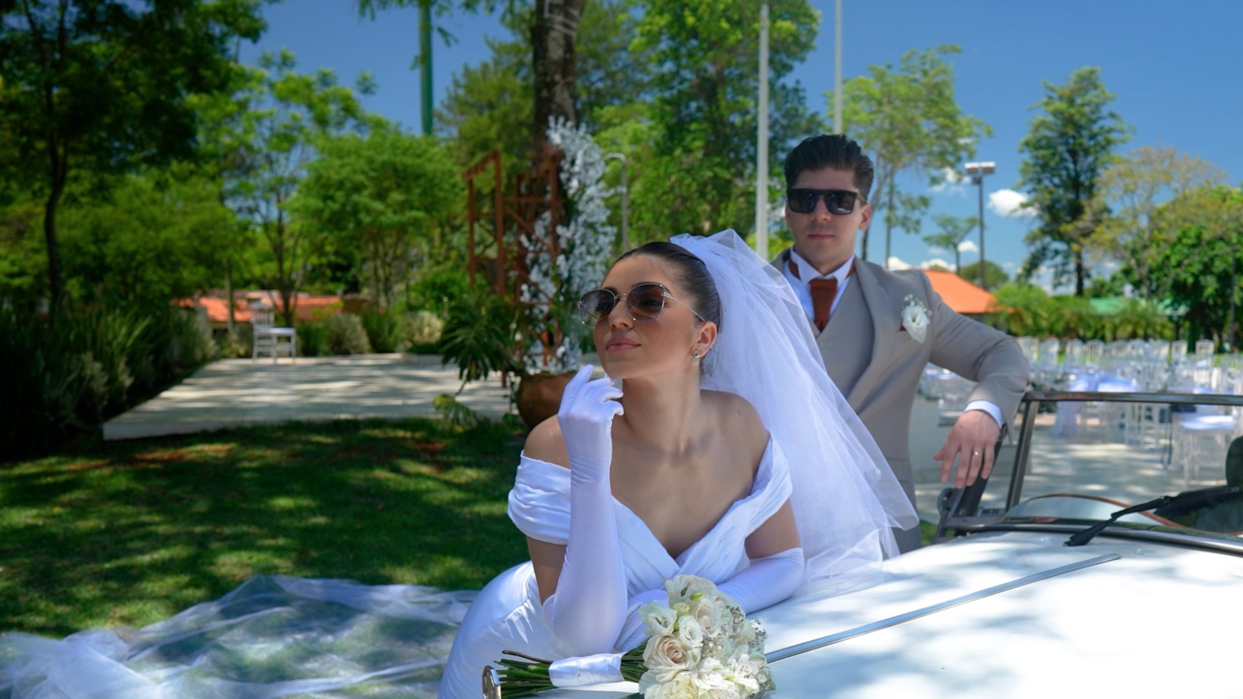 La novia con anteojos de sol y el velo sobre los hombros, en un jardín