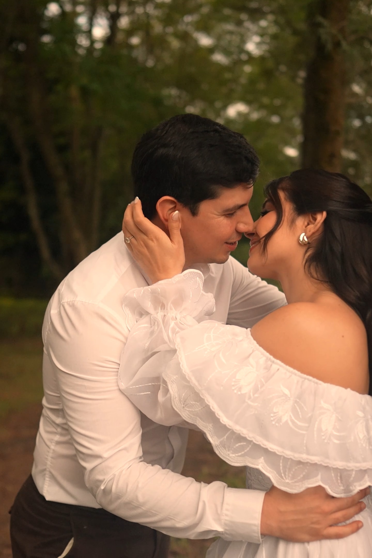 Los dos abrazados contra el tronco de un árbol, frente con frente, ella de vestido blanco de organza y él de camisa blanca