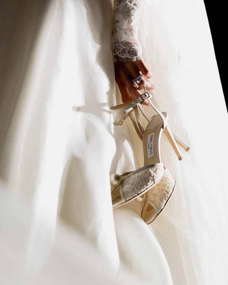 La mano de la novia sosteniendo sus sandalias de encaje contra el vestido blanco