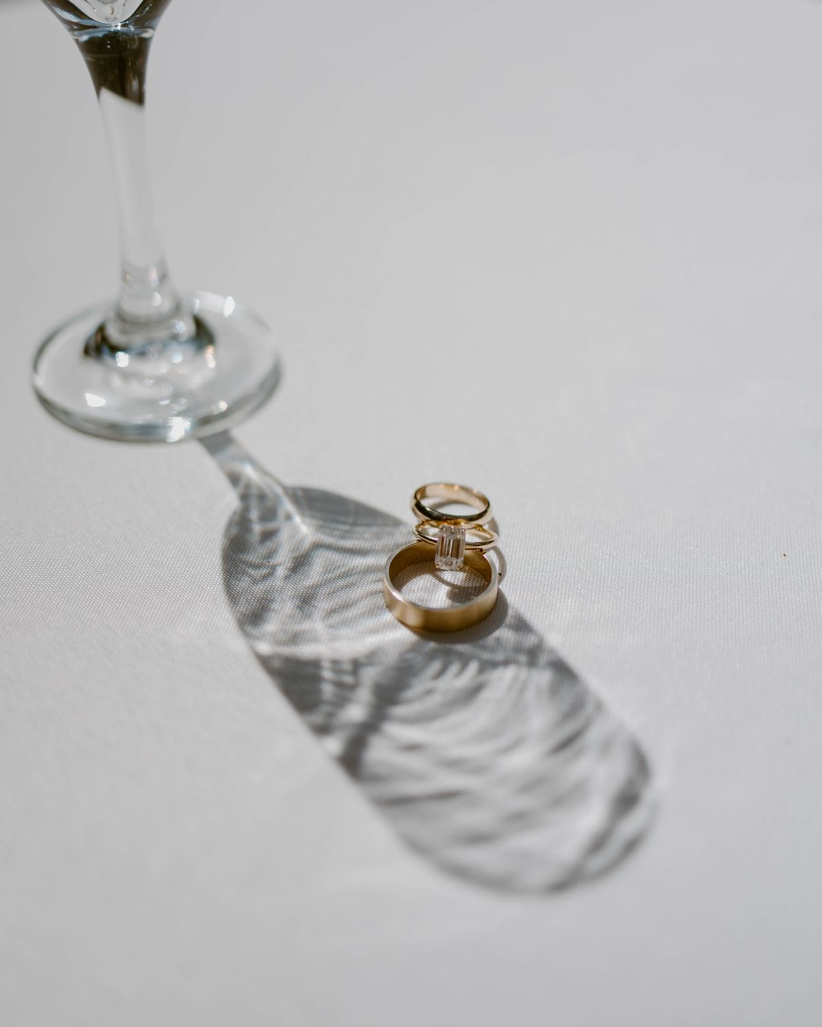 Los tres anillos de oro parados sobre el mantel blanco, con la sombra larga de una copa cruzando el cuadro
